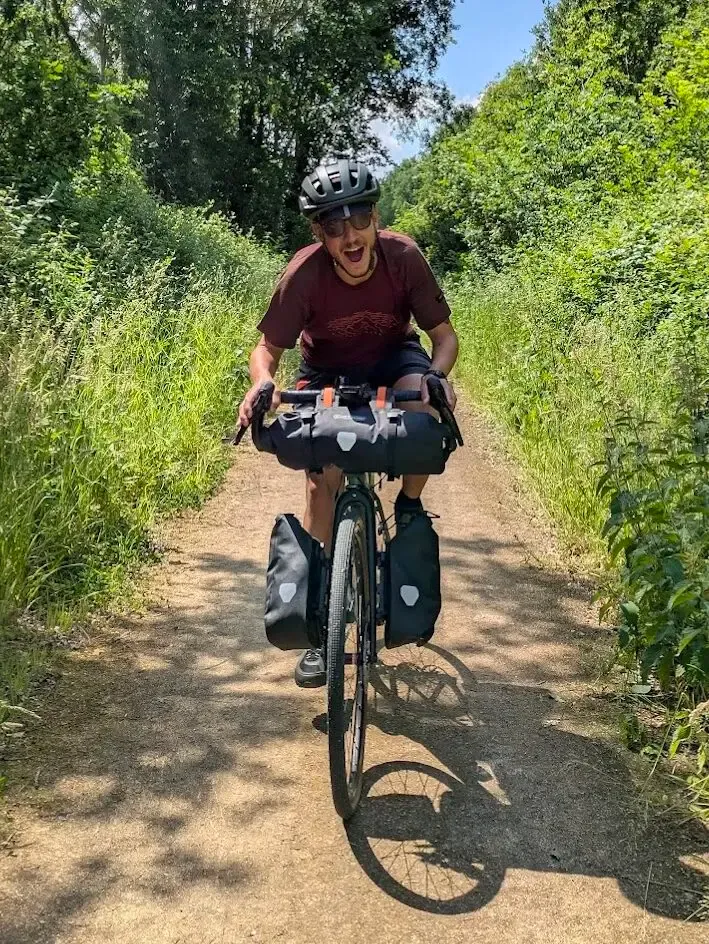 Cyclotouriste souriant sur une voie verte ombragée, sacoches chargées