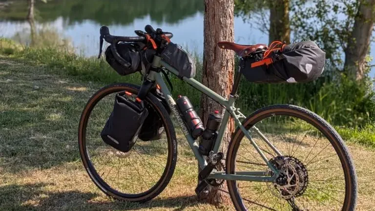 Vélo de voyage appuyé contre un arbre au bord d'un plan d'eau, au petit matin