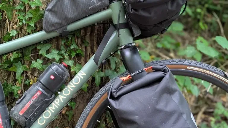Gros plan sur un vélo de voyage chargé de sacoches, adossé à un tronc d'arbre