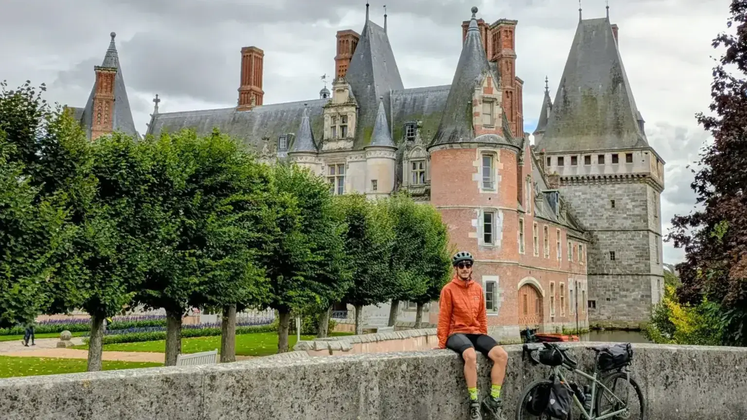 Cyclotouriste en pause sur un muret devant un château de la Loire, vélo chargé à côté
