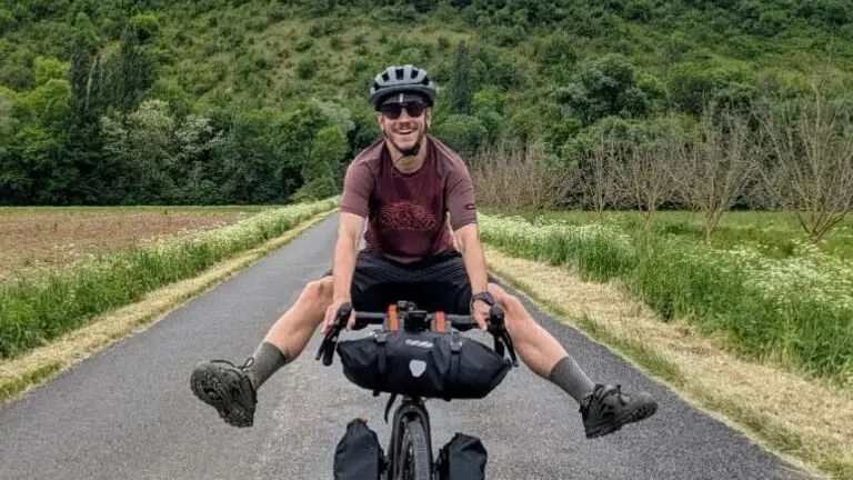 Cyclotouriste jambes tendues sur une route de plaine, falaises calcaires en arrière-plan